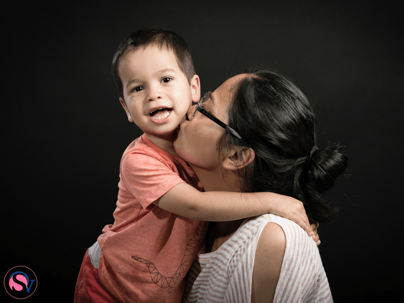 Woman kissing young boy on cheek against black background. An Aunt Writes