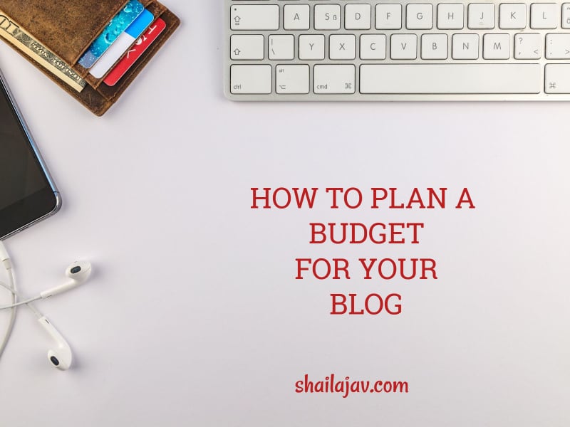 Laptop keys next to a wallet with credit cards and a pair of headphones. How to plan a blog budget and why you should.