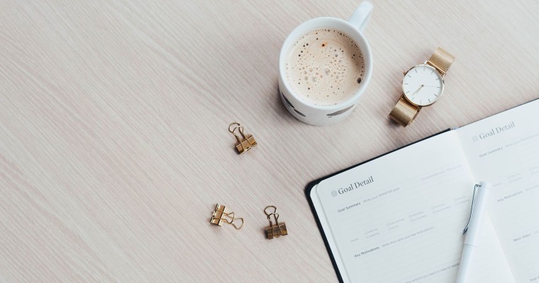 Flat lay of coffee cup, watch and planner on a desk indicating a morning routine