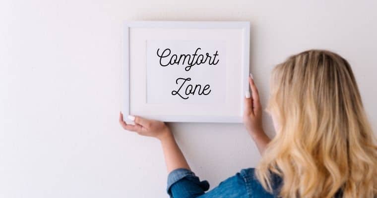 Woman hanging up a framed picture with the words comfort zone inside it