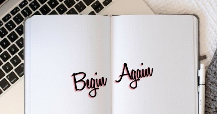 An open notebook open against a keyboard with the words Begin Again printed on the pages